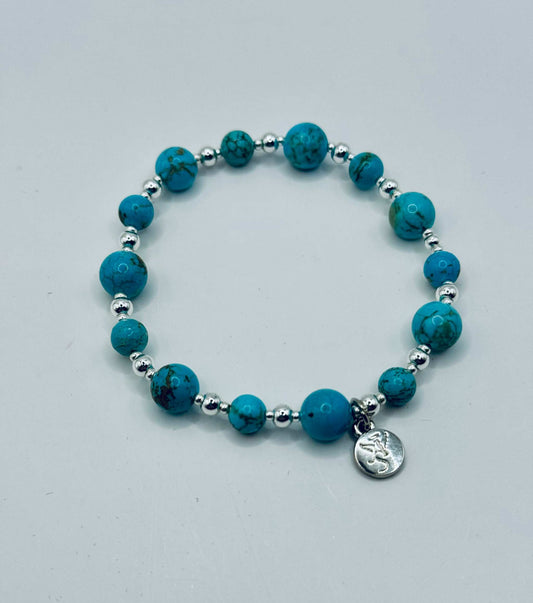 Turquoise bracelet with round blue beads and silver accents featuring a small silver charm.