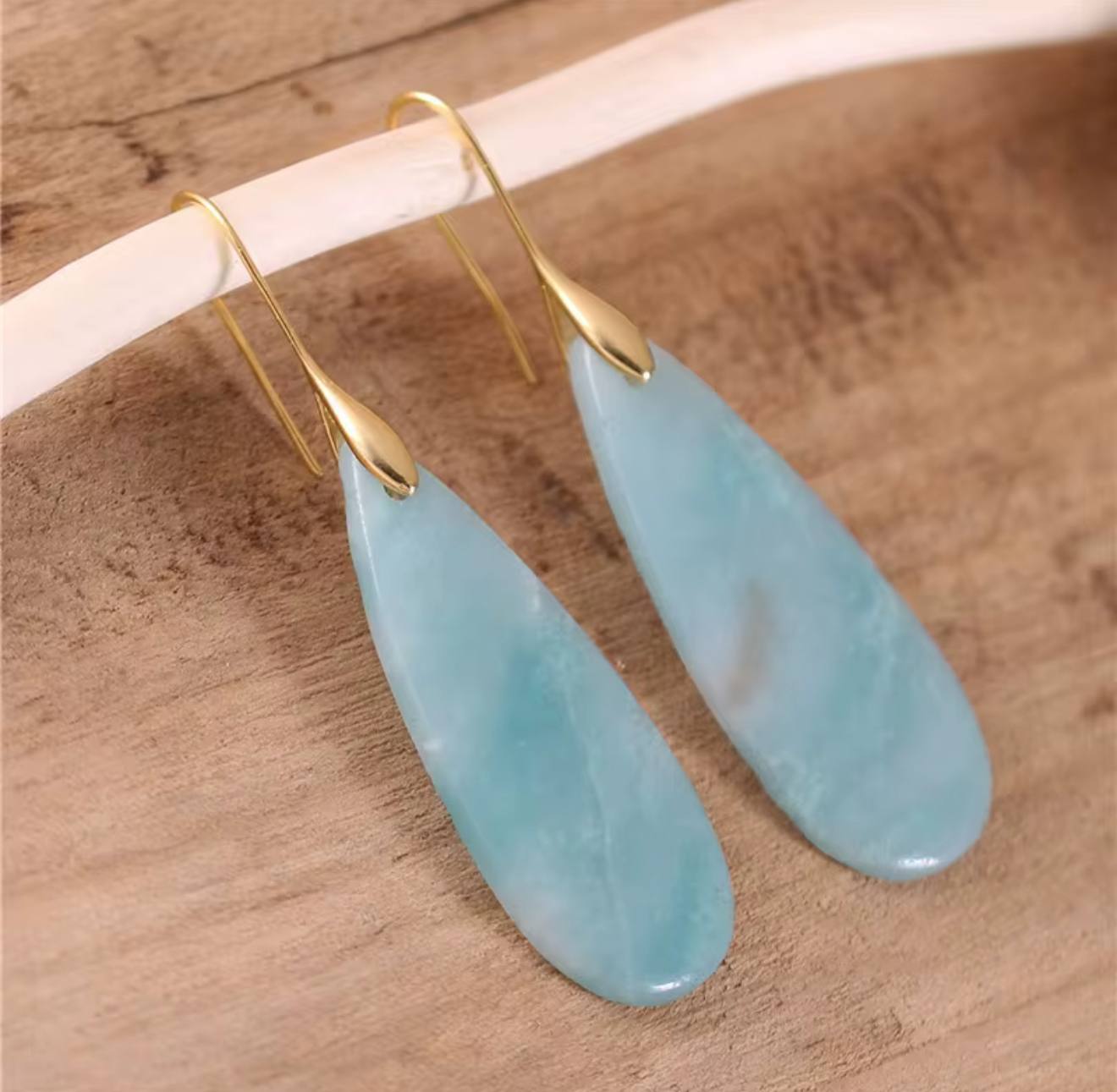 Sea Glass Calm Stone Drop Earrings with elongated aqua teardrop stones and gold-tone hooks on wooden background