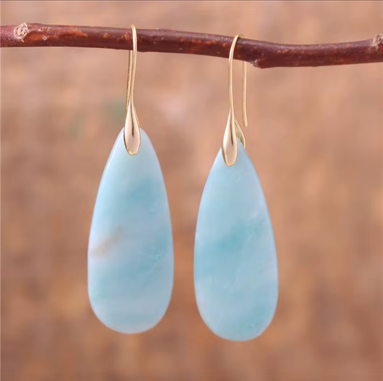 Sea Glass Calm Stone Drop Earrings with elongated aqua teardrop stones on gold-tone hooks hanging from a twig.