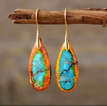 Sunfire Tide Jasper Drop Earrings with vibrant multicolored jasper teardrop stones and gold-tone hooks hanging on a wooden branch